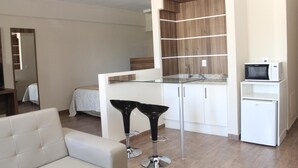Un espacio habitable moderno y funcional, con kitchenette, mesa de comedor con cubierta de vidrio y un refrigerador pequeño.