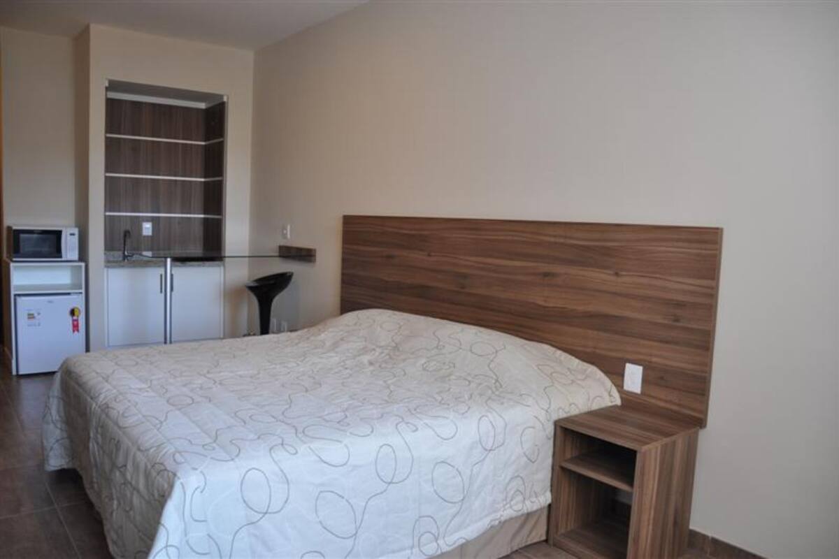 A bedroom with a wooden headboard, a bed with a patterned bedspread, a small bedside table, and a built-in wardrobe with shelves.