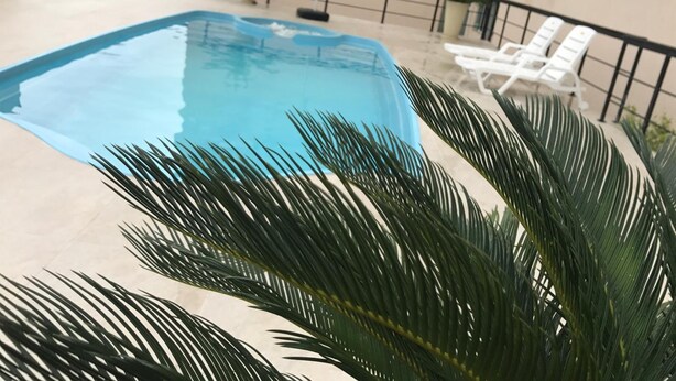 Una piscina con una sombrilla blanca, rodeada de palmeras y sillas de descanso blancas.