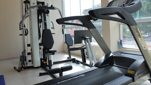 Un gimnasio con cinta de correr, máquinas de pesas y una ventana con vista a edificios.