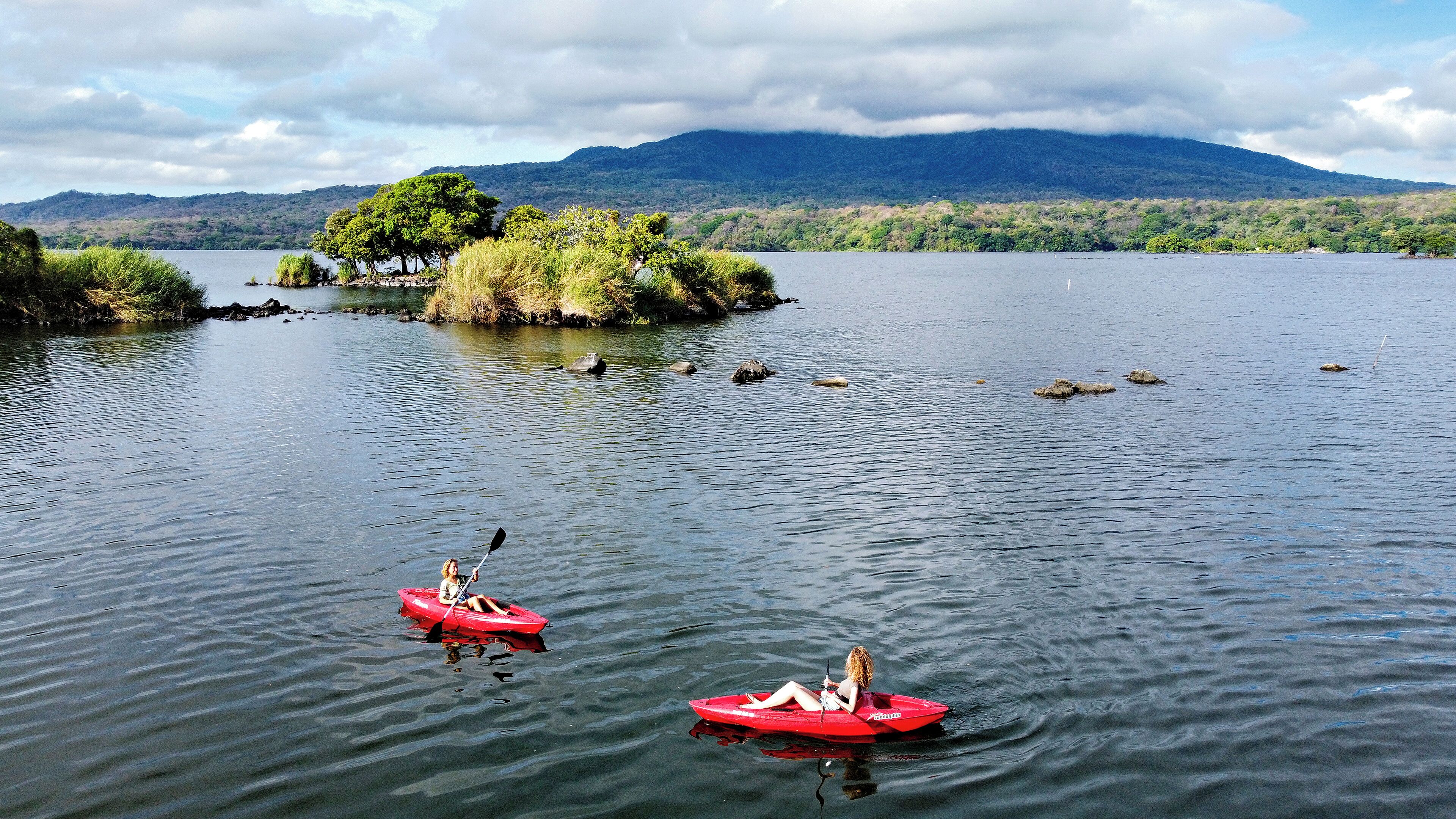 Un lago tranquilo con dos kayaks rojos, un cielo despejado y una montaña al fondo.