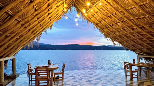 A thatched-roof outdoor seating area with a view of a calm body of water and distant hills. - Isleta El Espino Ecolodge (Granada)