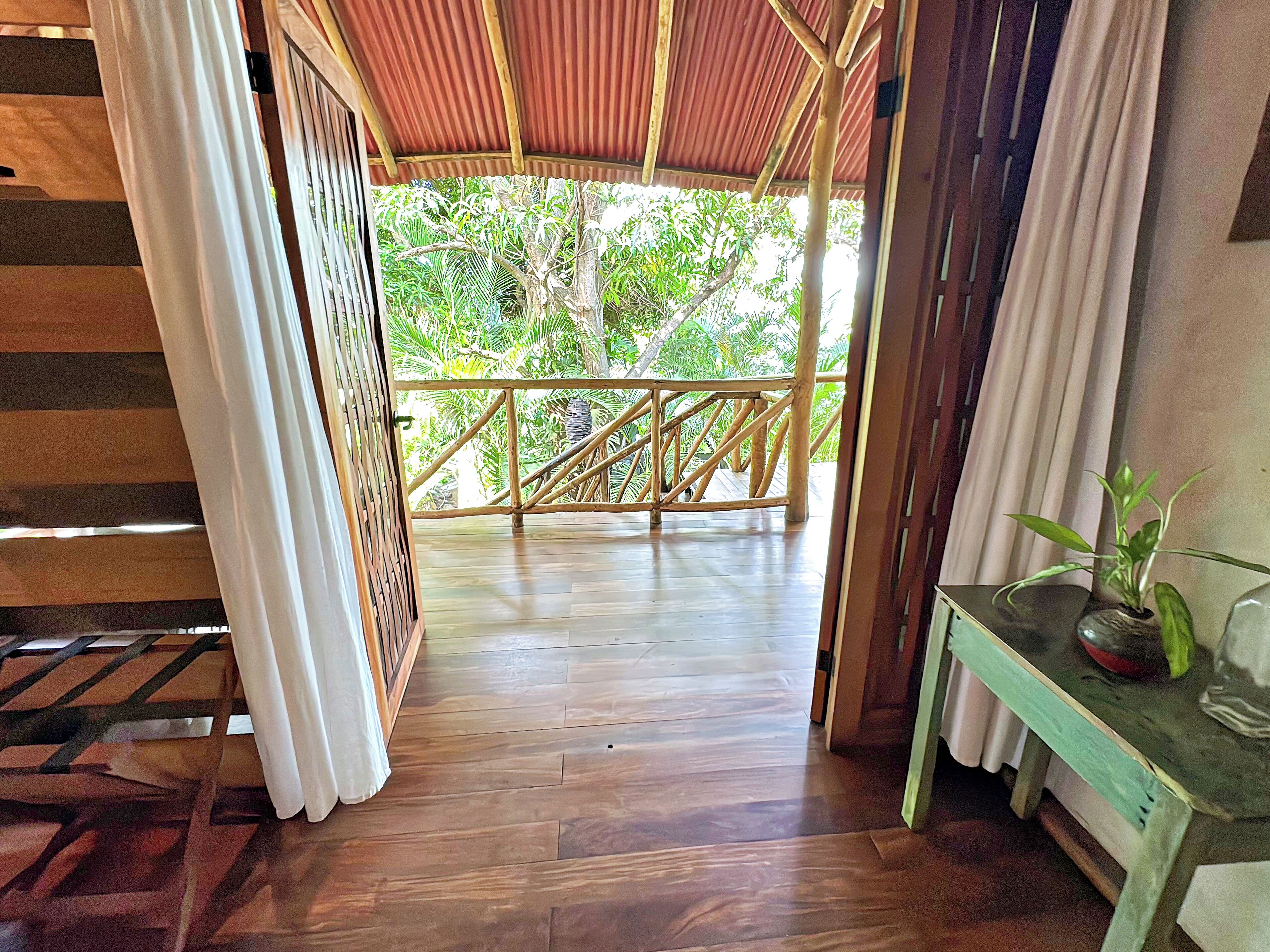 A wooden deck with a bamboo railing, leading to a covered area with a corrugated metal roof.