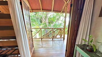 A wooden deck with a bamboo railing, leading to a covered area with a corrugated metal roof.