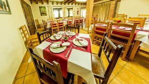 A dining area with wooden tables and chairs, red tablecloths, and a brick wall. - Hotel Rural La Noria (Ciudad Rodrigo)