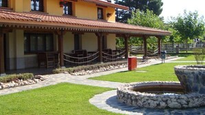 A building with a tiled roof, a covered patio with seating, and a stone water feature. - Hotel Rural La Noria (Ciudad Rodrigo)
