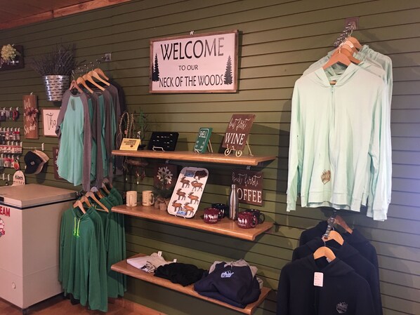 Un magasin de vêtements avec une enseigne indiquant « Bienvenue dans notre quartier », des étagères remplies de vêtements, et des panneaux indiquant « D’abord, un verre de vin » et « D’abord, un café ».