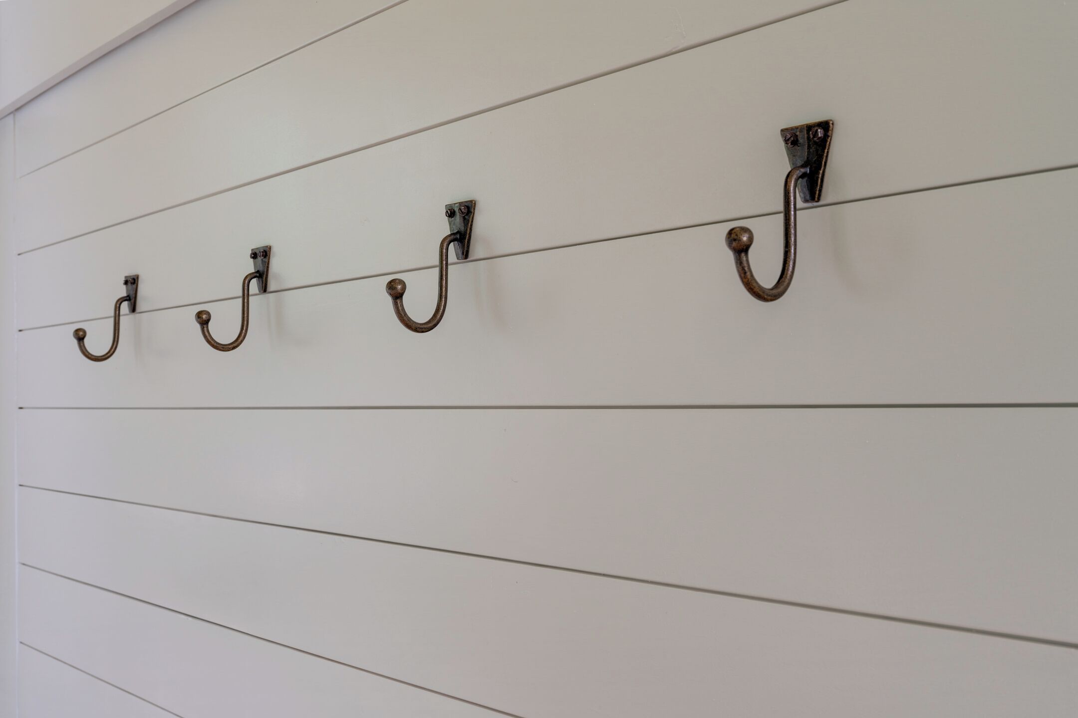 Una pared con líneas horizontales y cuatro ganchos metálicos alineados.