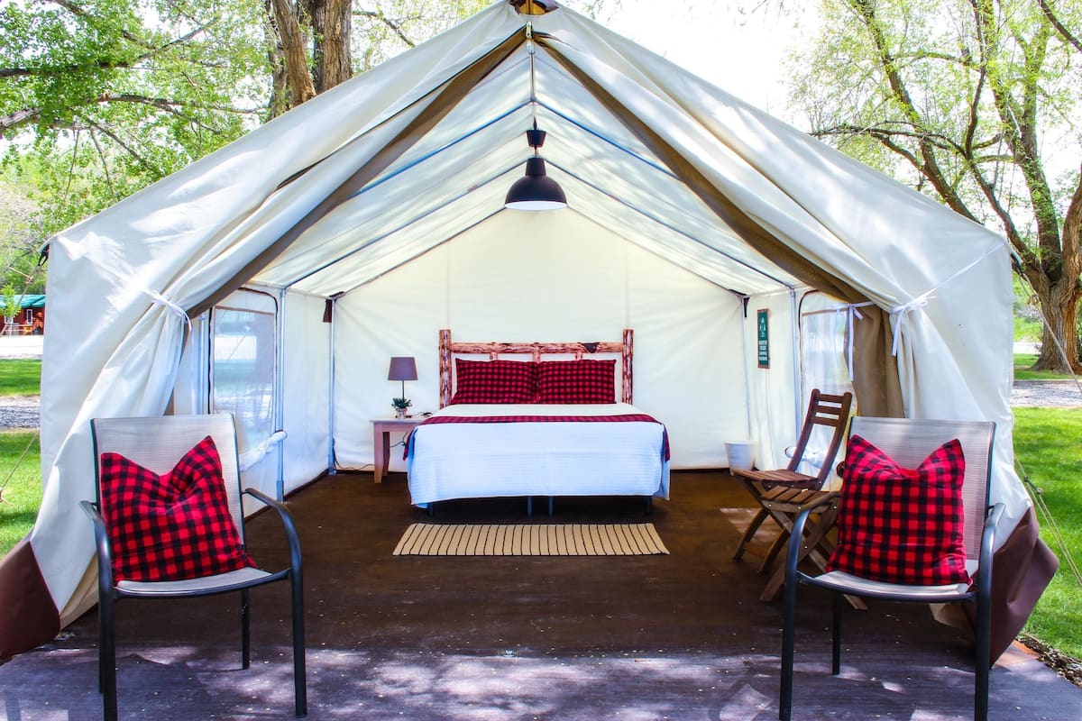 A tent with a bed, two chairs, and a hanging light fixture.