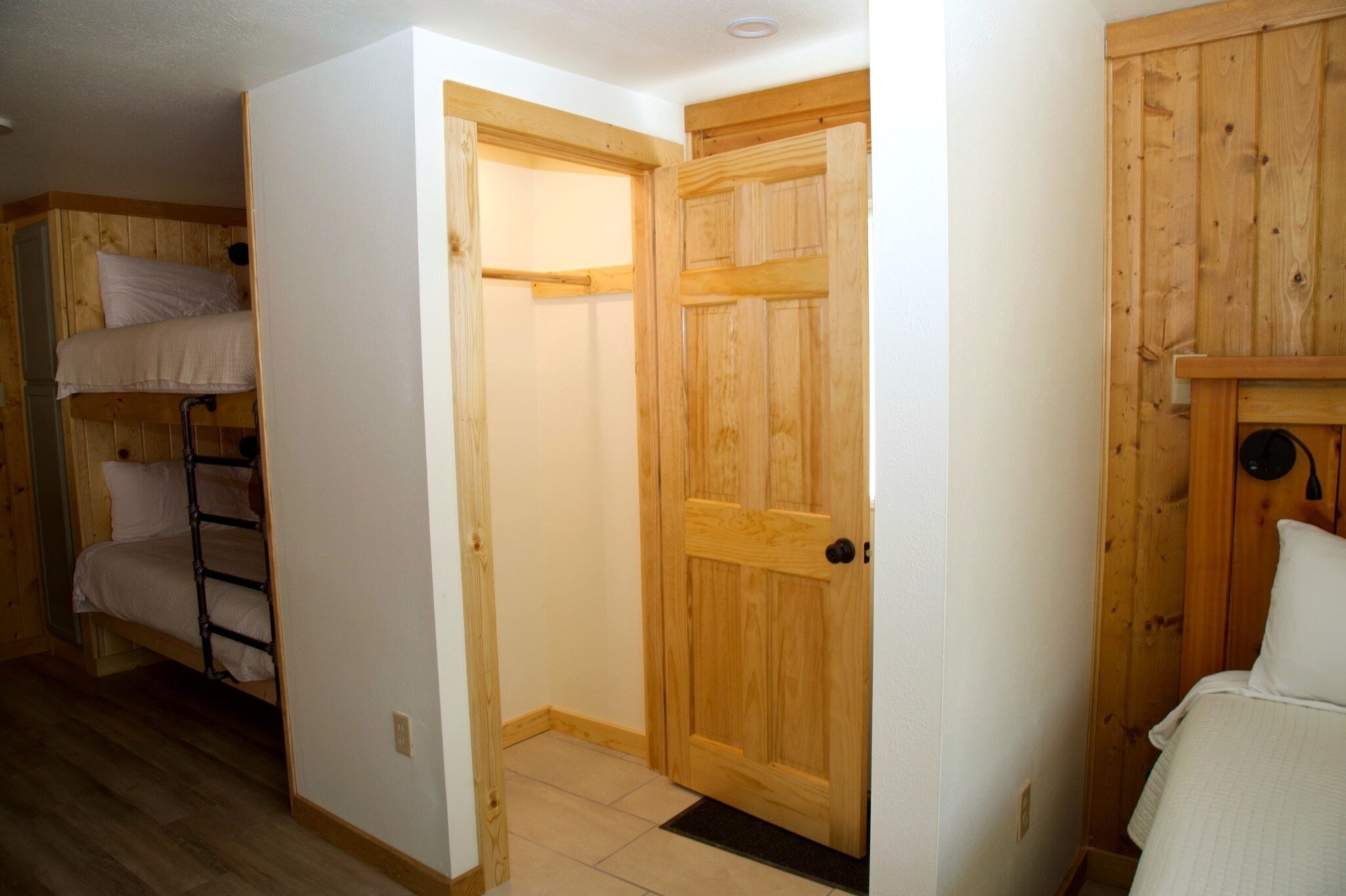 Une chambre avec un lit superposé, une porte en bois et un petit placard.