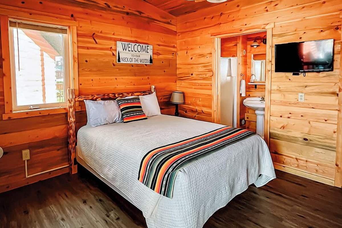 A wooden cabin bedroom with a bed, a ceiling fan, a TV, and a window.