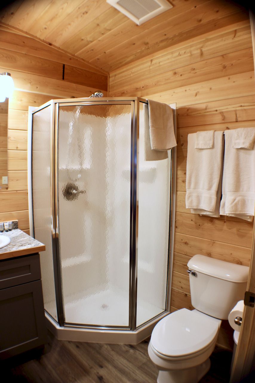 Un baño con paneles de madera, una ducha con cerramiento de vidrio, un inodoro y un lavabo.