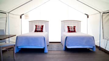 A tented accommodation with two beds, each with a pillow, a small table, and a chair.