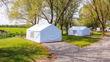 Two white tents in a grassy area with trees, a gravel path, and a picnic table in the background.