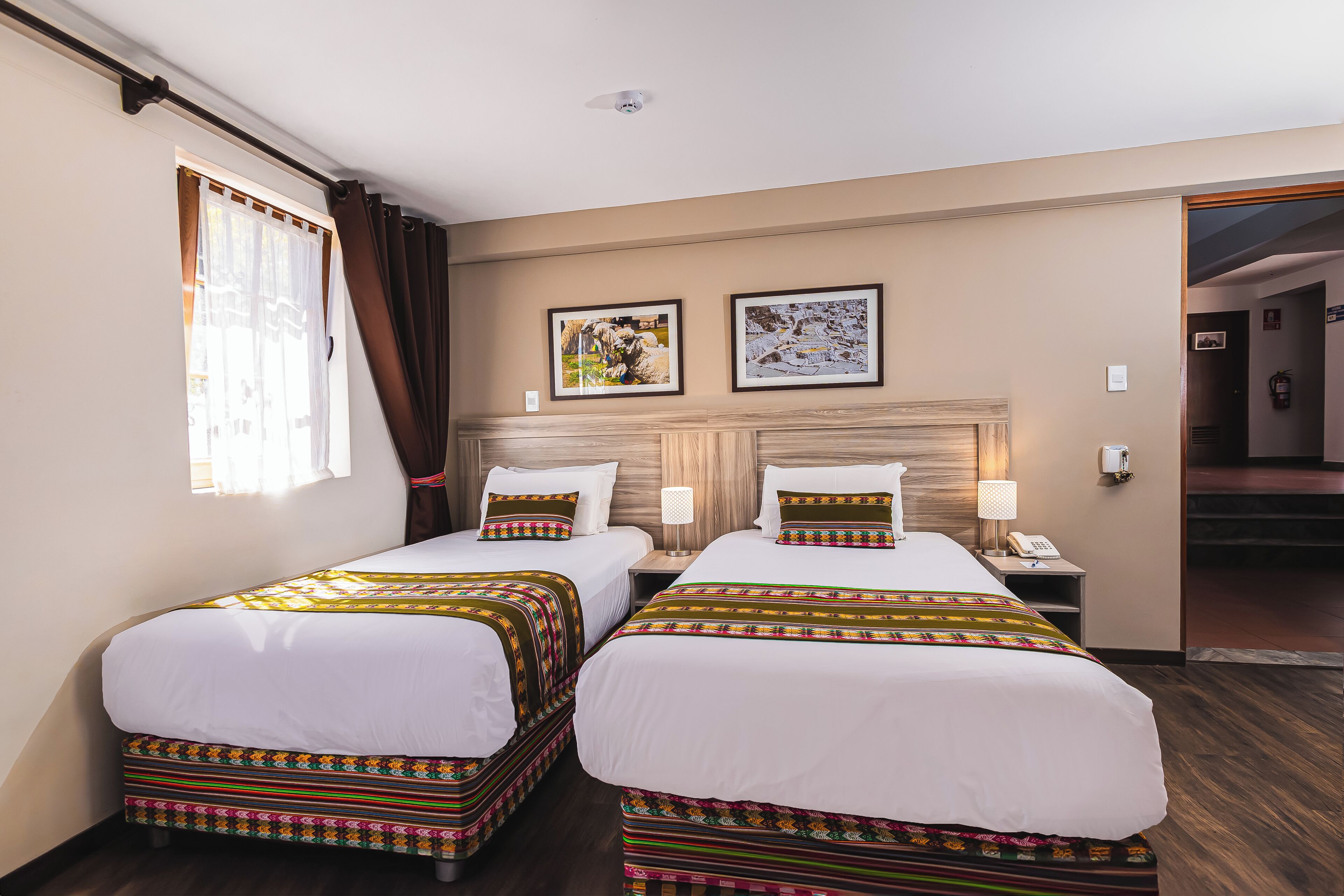 A hotel room with two beds, a window with curtains, a headboard, and two framed pictures on the wall.