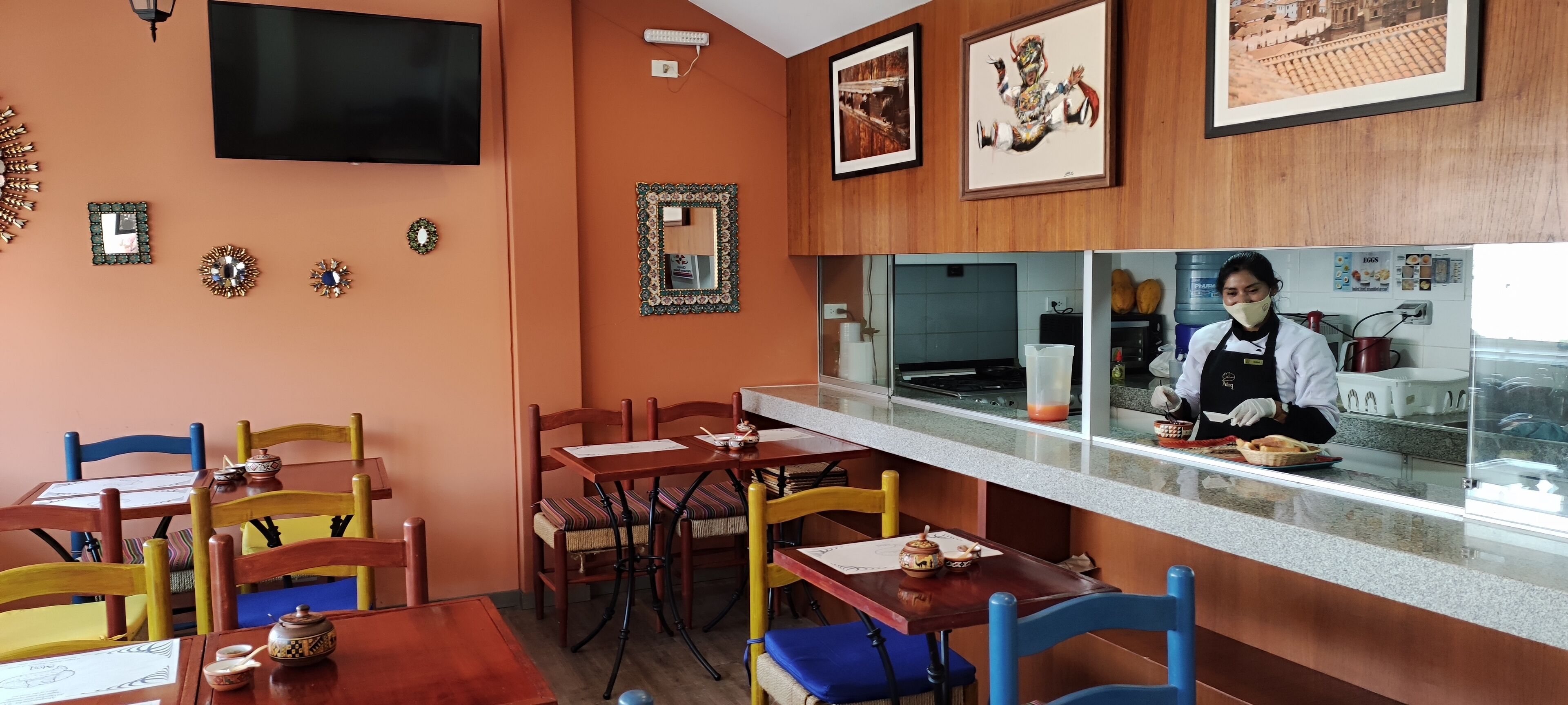 Un interior de restaurante con paredes de madera, una barra donde trabaja un chef y varias mesas con sillas.