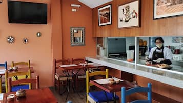 A restaurant interior with wooden walls, a counter with a chef, and several dining tables with chairs.