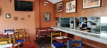 A restaurant interior with wooden walls, a counter with a chef, and several dining tables with chairs.