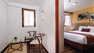 Habitación de hotel con cama, una mesita con una planta, dos sillas y una ventana.