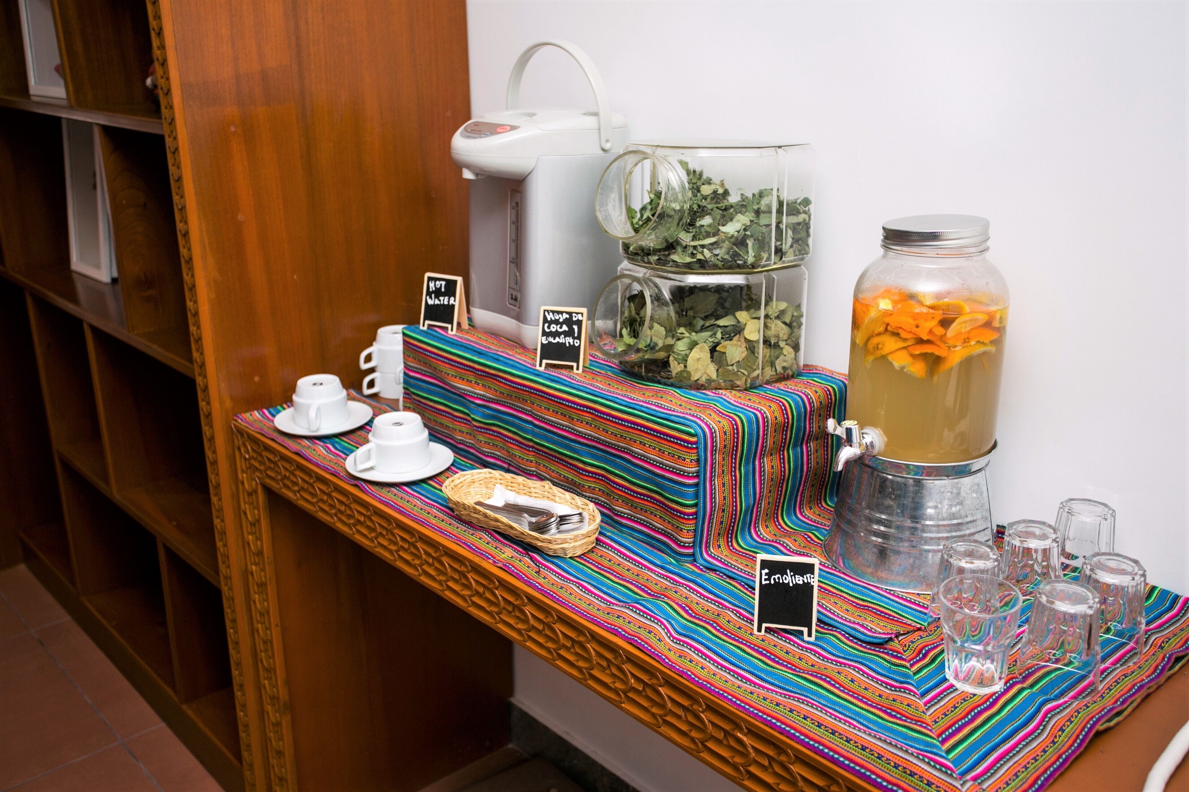 A buffet setup with a coffee maker, a large pitcher of tea, and a jar of orange slices.