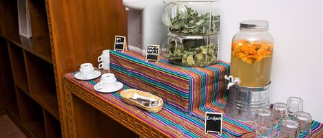 A buffet setup with a coffee maker, a large pitcher of tea, and a jar of orange slices.
