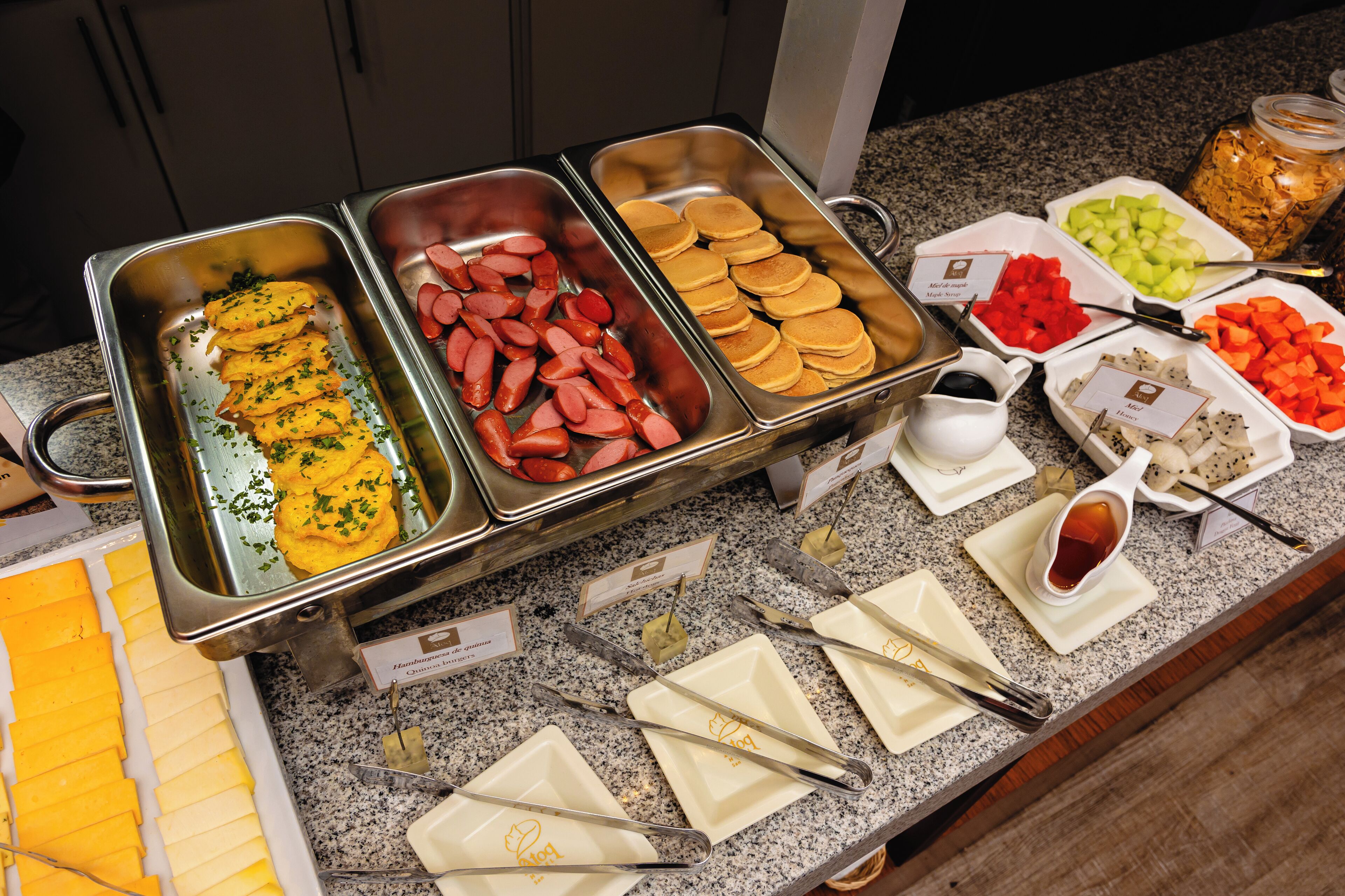 A buffet with various food items including cheese, sausages, pancakes, and fruits.