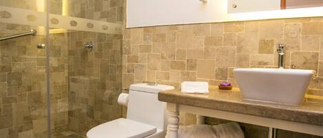A bathroom with a glass-enclosed shower, a white toilet, a sink with a mirror above it, and a tiled floor.