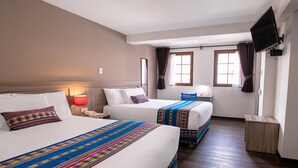 Una habitación de hotel con dos camas, un televisor montado en la pared y una ventana con cortinas.