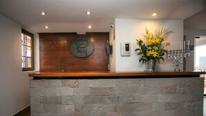 A reception area with a stone counter, a wooden wall with a logo, a wall-mounted phone, a flower arrangement, and a menorah. - Atoq San Blas Hotel (Cusco)