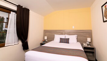 Habitación de hotel con cama, dos mesitas de noche, un teléfono montado en la pared y una ventana con cortinas.