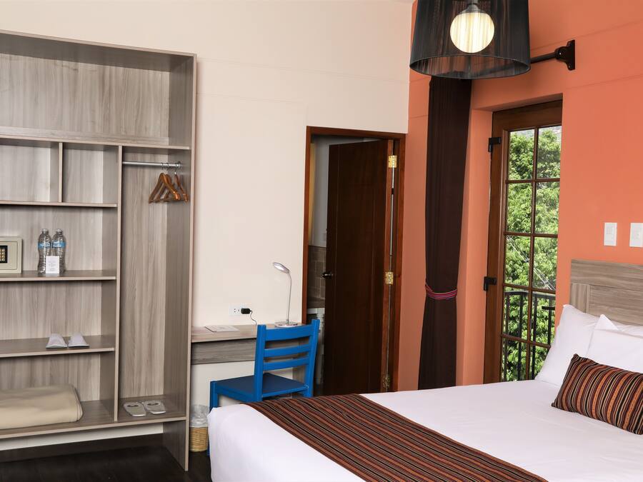Habitación de hotel con cama, escritorio, armario y ventana con vistas a zonas verdes.