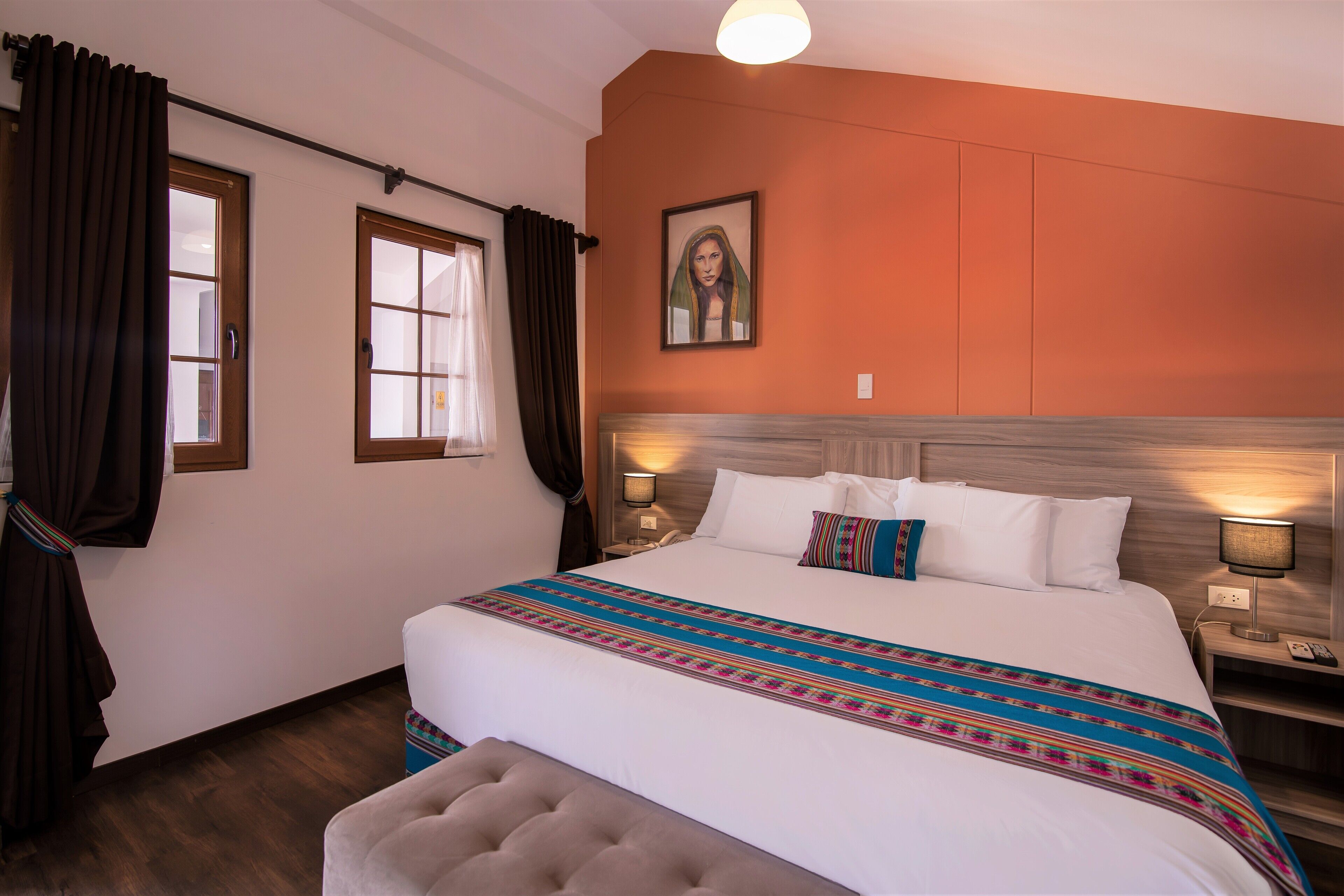 A hotel room with a large bed, two bedside lamps, a headboard, a window with curtains, and a wall-mounted painting.