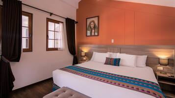 A hotel room with a large bed, two bedside lamps, a headboard, a window with curtains, and a wall-mounted painting.