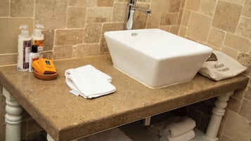 Une salle de bain avec un lavabo blanc, des articles de toilette et des serviettes posés sur un comptoir en pierre.