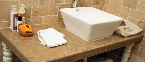 Un baño con un lavabo blanco, artículos de aseo y toallas sobre una encimera de piedra.