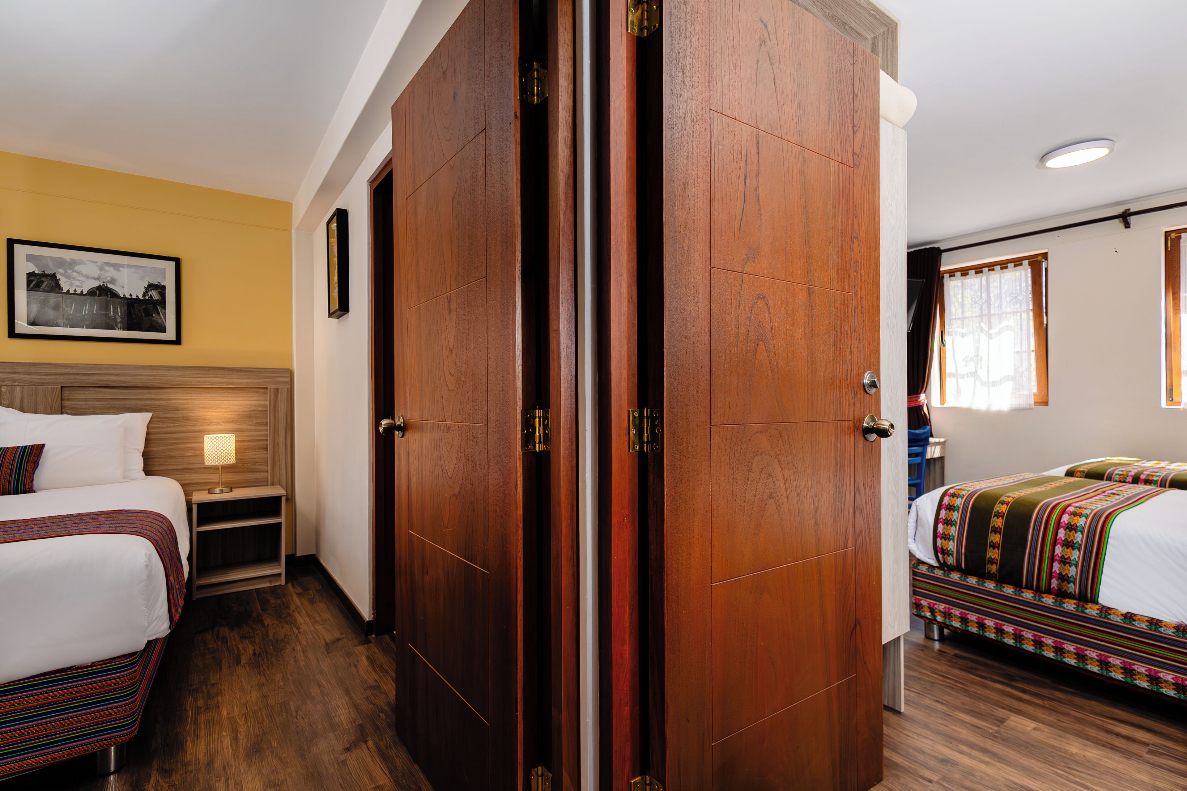 Habitación de hotel con dos camas, un armario de madera y una mesita de noche con lámpara.
