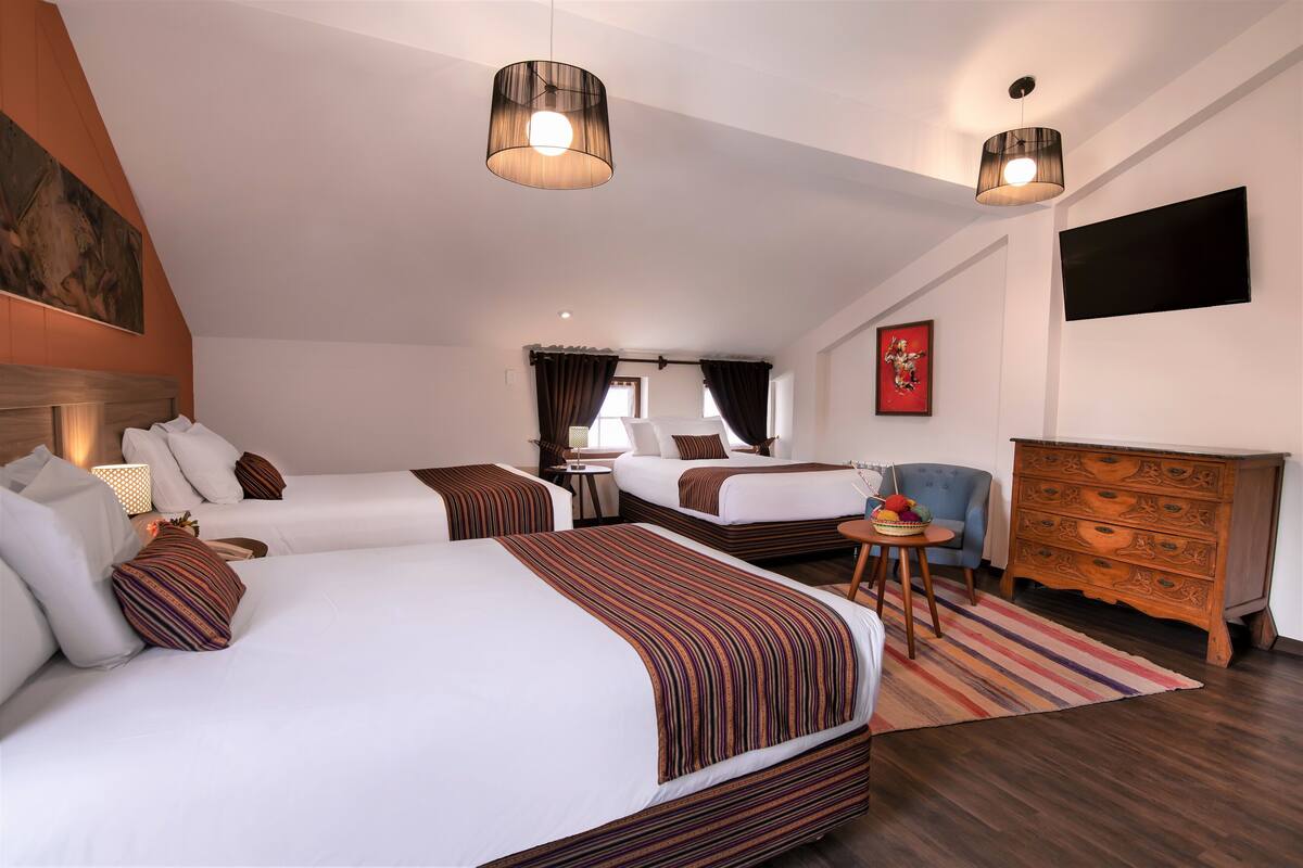 Une chambre d’hôtel avec deux lits, une commode en bois, une télévision et une petite table avec une lampe.