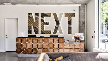 Un espace d’accueil avec une grande enseigne « NEXT », un comptoir en bois et un canapé avec des coussins.