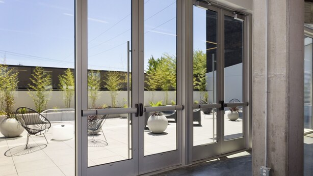 A modern building entrance with large glass doors, outdoor seating, and potted plants. - Jupiter NEXT (Portland)