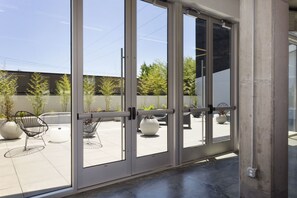 Entrada de un edificio moderno con puertas de vidrio grandes, asientos exteriores y plantas en macetas.
