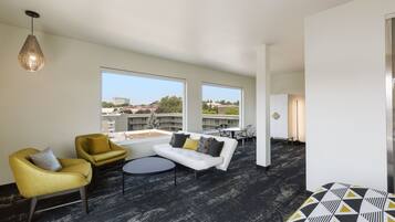 A modern lounge area with a white sofa, yellow armchairs, and a round table. Large windows offer a view of the cityscape.