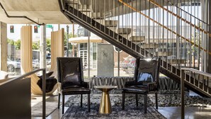 A modern lobby with a staircase, two leather chairs, a round table, and a view of the street outside. - Jupiter NEXT (Portland)
