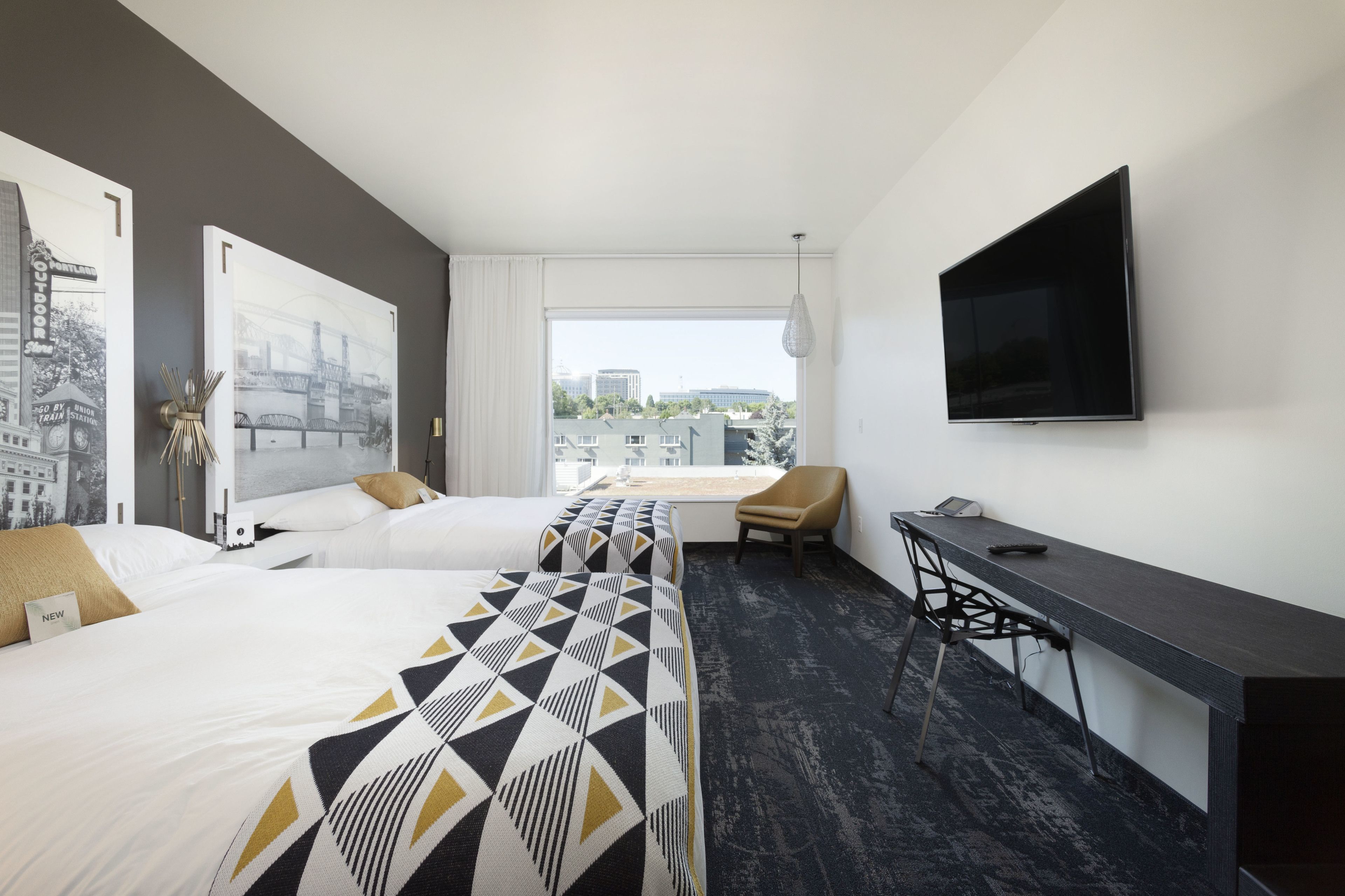 A hotel room with two beds, a desk, a chair, and a TV.