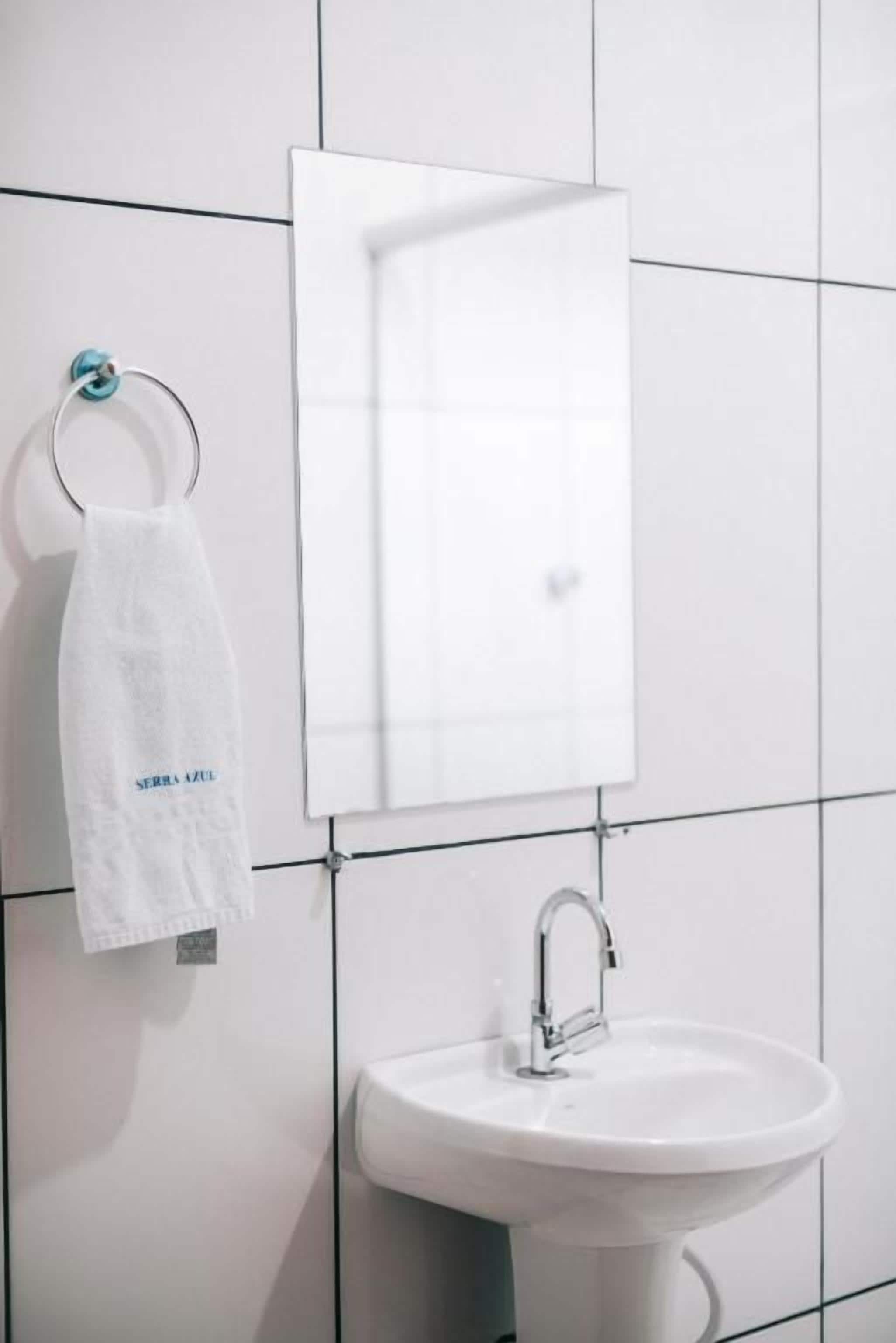 Une salle de bain avec un lavabo blanc, une serviette suspendue à un anneau en métal et un miroir au-dessus du lavabo.