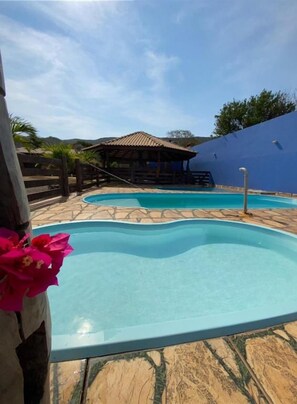 Una piscina con cubierta de madera, un área de estar techada y vista al mar.