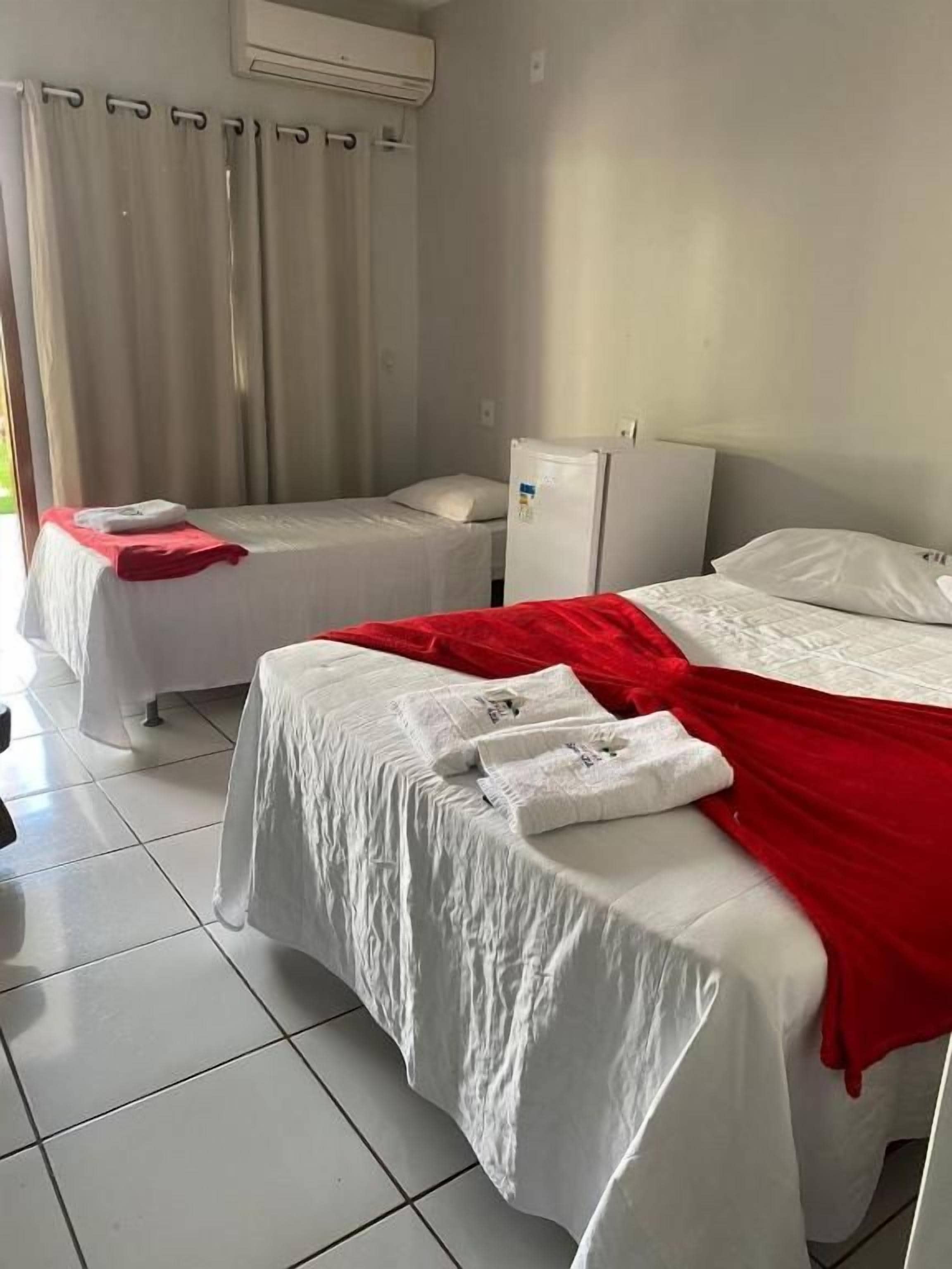 A hotel room with two beds, a small refrigerator, and a window with curtains.
