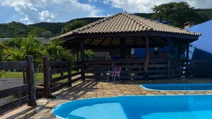 Zona de piscina con solárium empedrado, valla de madera y pabellón cubierto.