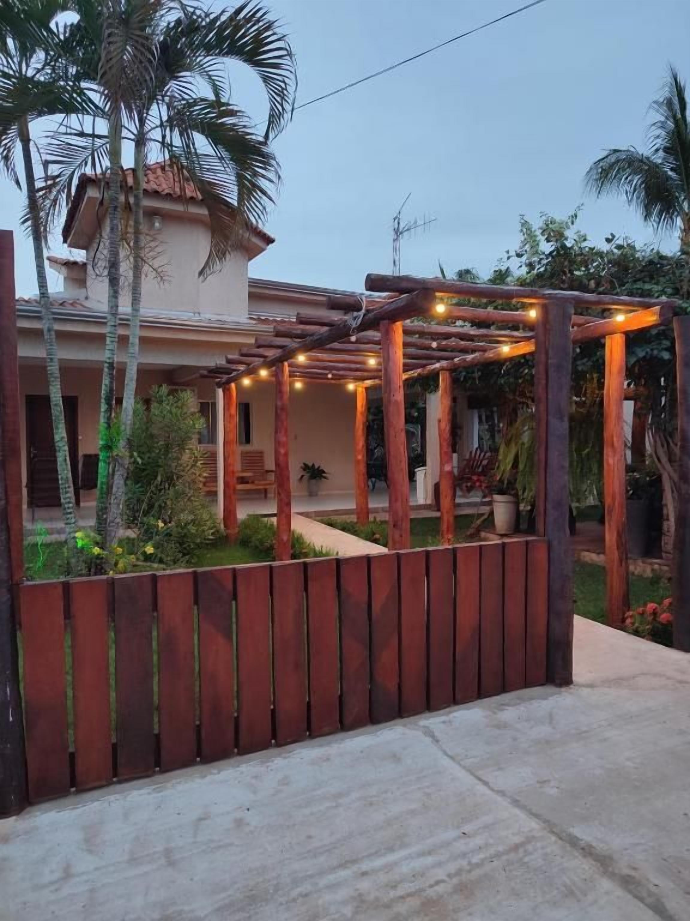 A wooden pergola with string lights, a concrete pathway, and a wooden fence.