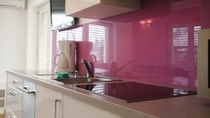 A modern kitchen with a stainless steel sink, white cabinets, and a pink backsplash.