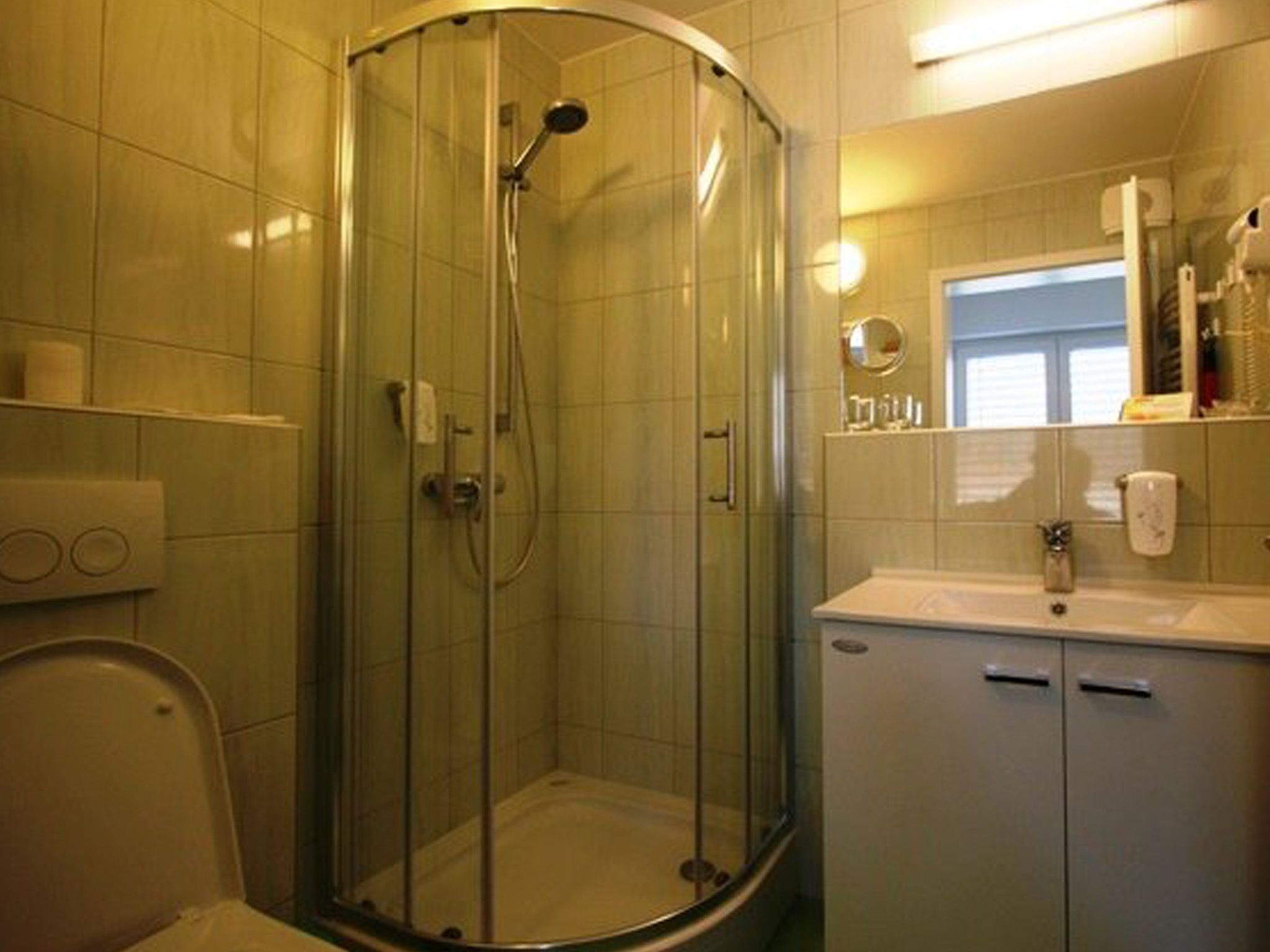 A bathroom with a glass-enclosed shower, a toilet, a sink with a mirror, and a cabinet.